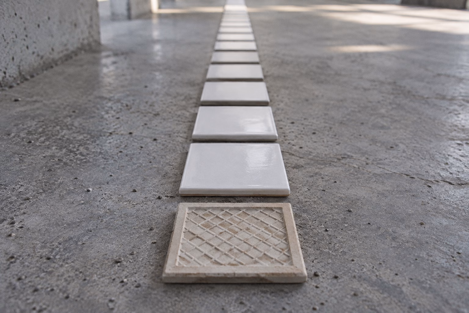 A long row of identical white ceramic tiles laid in a line on grey concrete, the nearest tile turned face down
