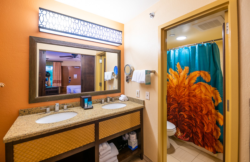 Hotel room bath area with a double vanity, large mirror, and sliding door