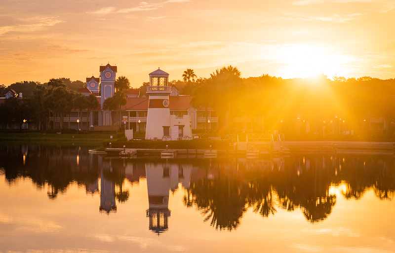 Warm sunrise over a lighthouse and pastel resort buildings beside the Caribbean Beach waterfront