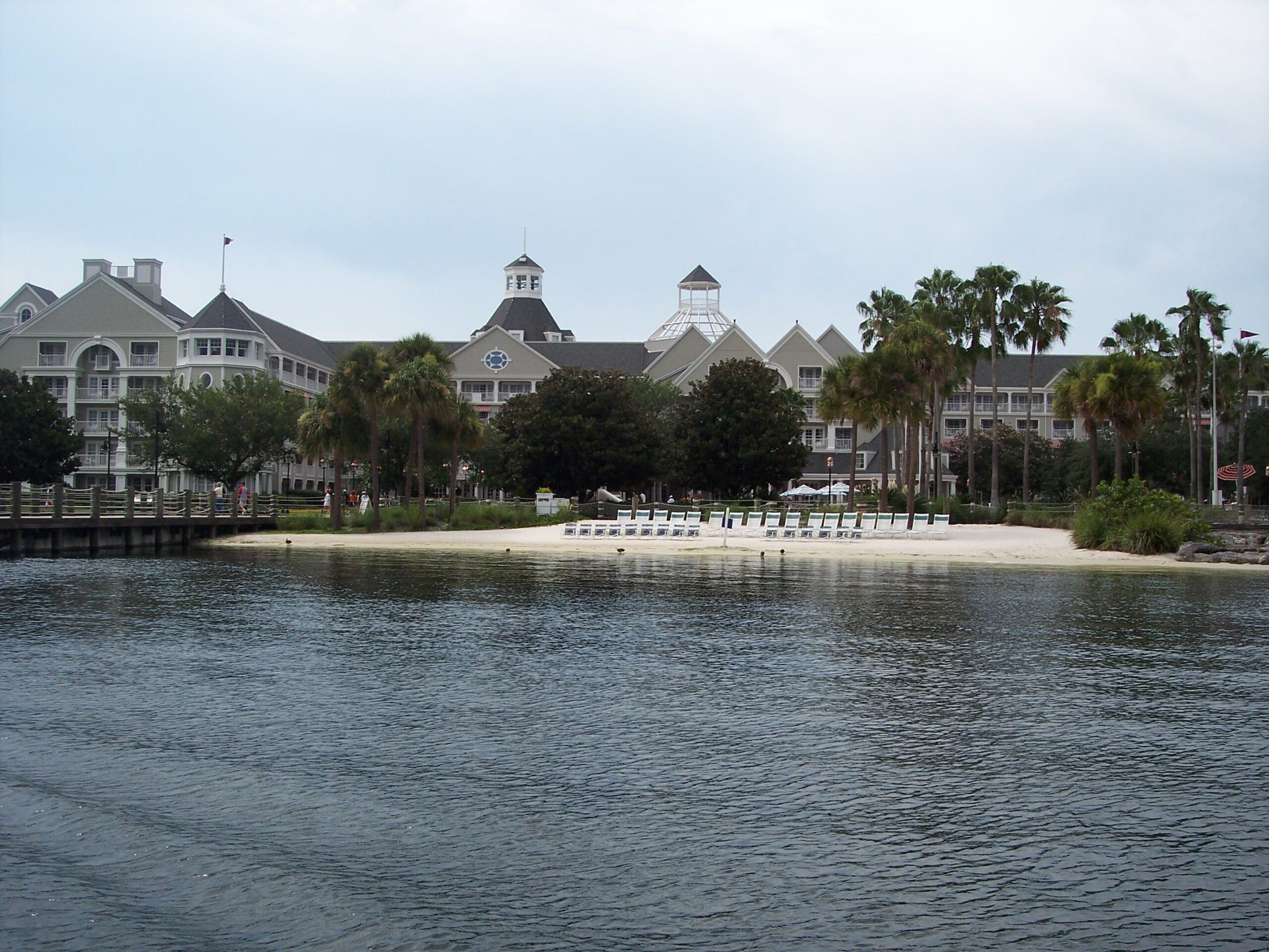 A view of Disney's Yacht Club Resort with its distinctive architecture, palm trees, and a sandy beach area in the foreground. The resort's exterior features a n