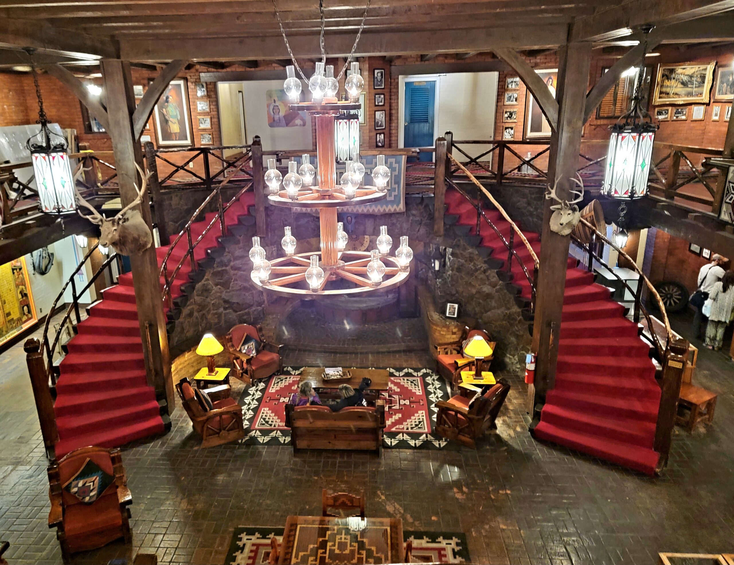 A grand interior view of Hotel El Rancho featuring a central staircase with a rustic design, surrounded by wooden beams and adorned with Native American-style m