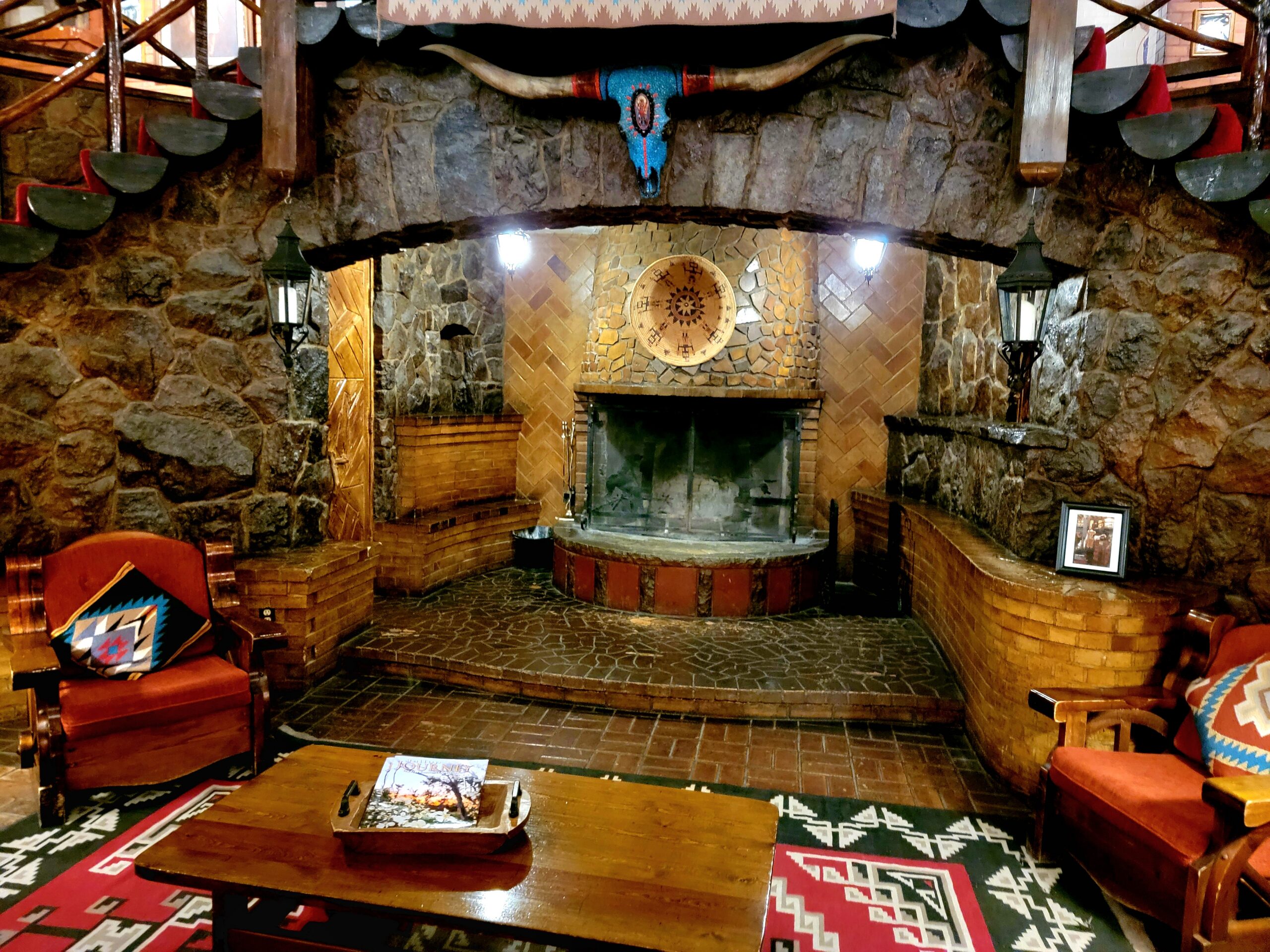 A cozy fireplace with a stone surround and decorative elements, surrounded by seating and a patterned rug, reflecting the rustic and traditional ambiance of the