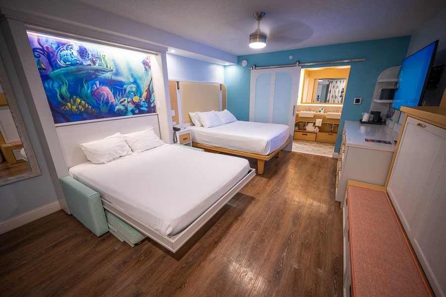 Disney resort room with two beds, blue walls, wood-look flooring, and Little Mermaid artwork