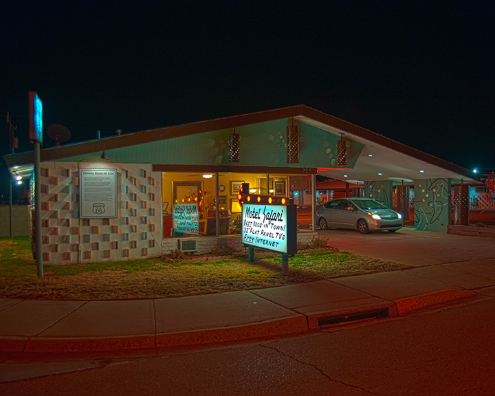 A nighttime view of Motel Safari, showcasing its exterior with a sign indicating amenities such as 'Best beds in town!', '32
