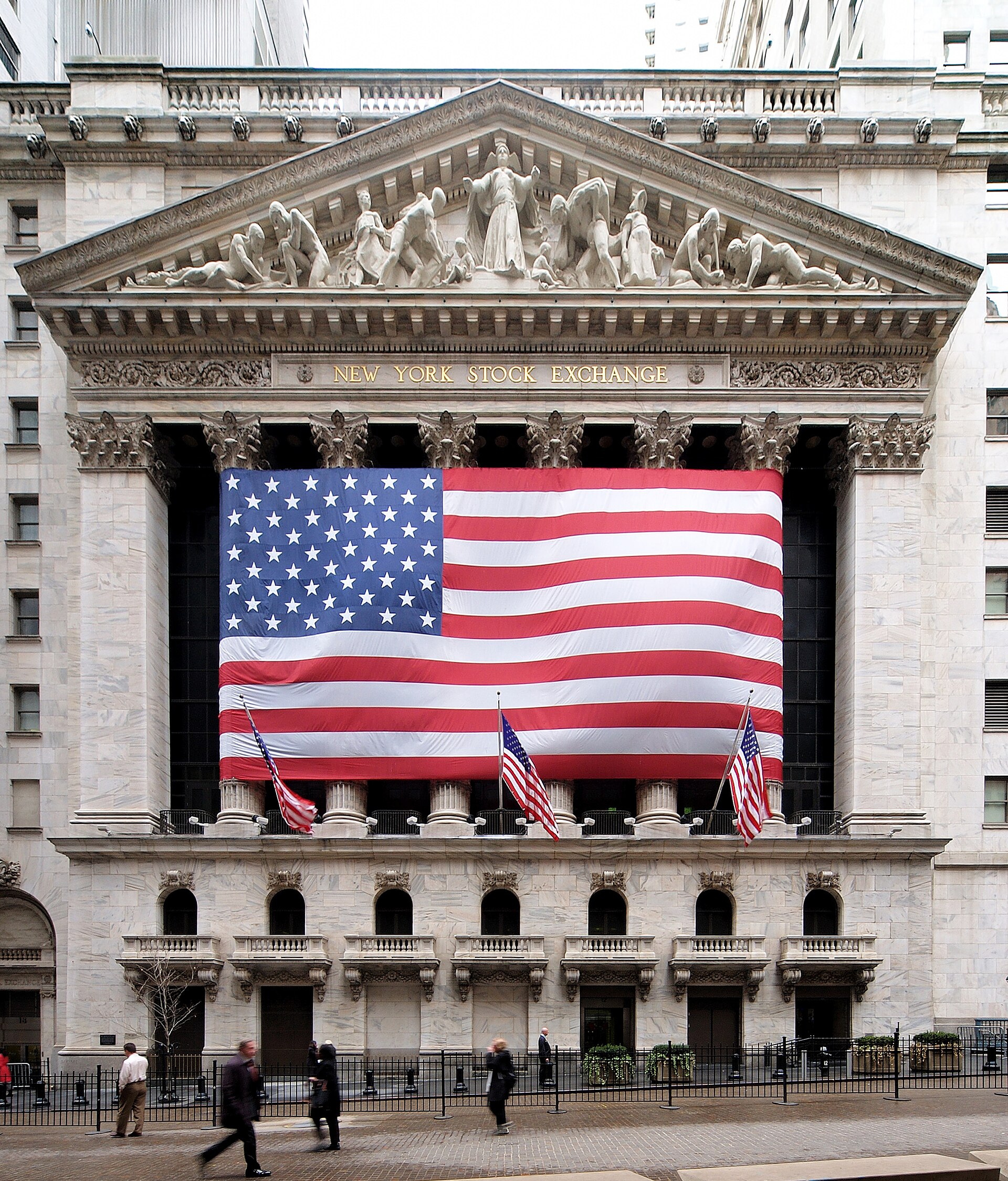 Front of the New York Stock Exchange building with a large United States flag hanging between its columns