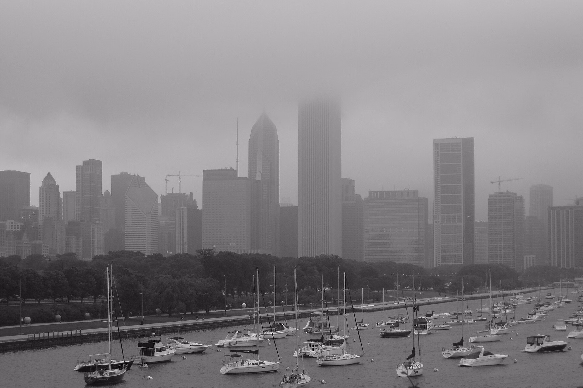 Low grey cloud swallowing the upper floors of downtown Chicago skyscrapers above a harbour crowded with moored sailboats.