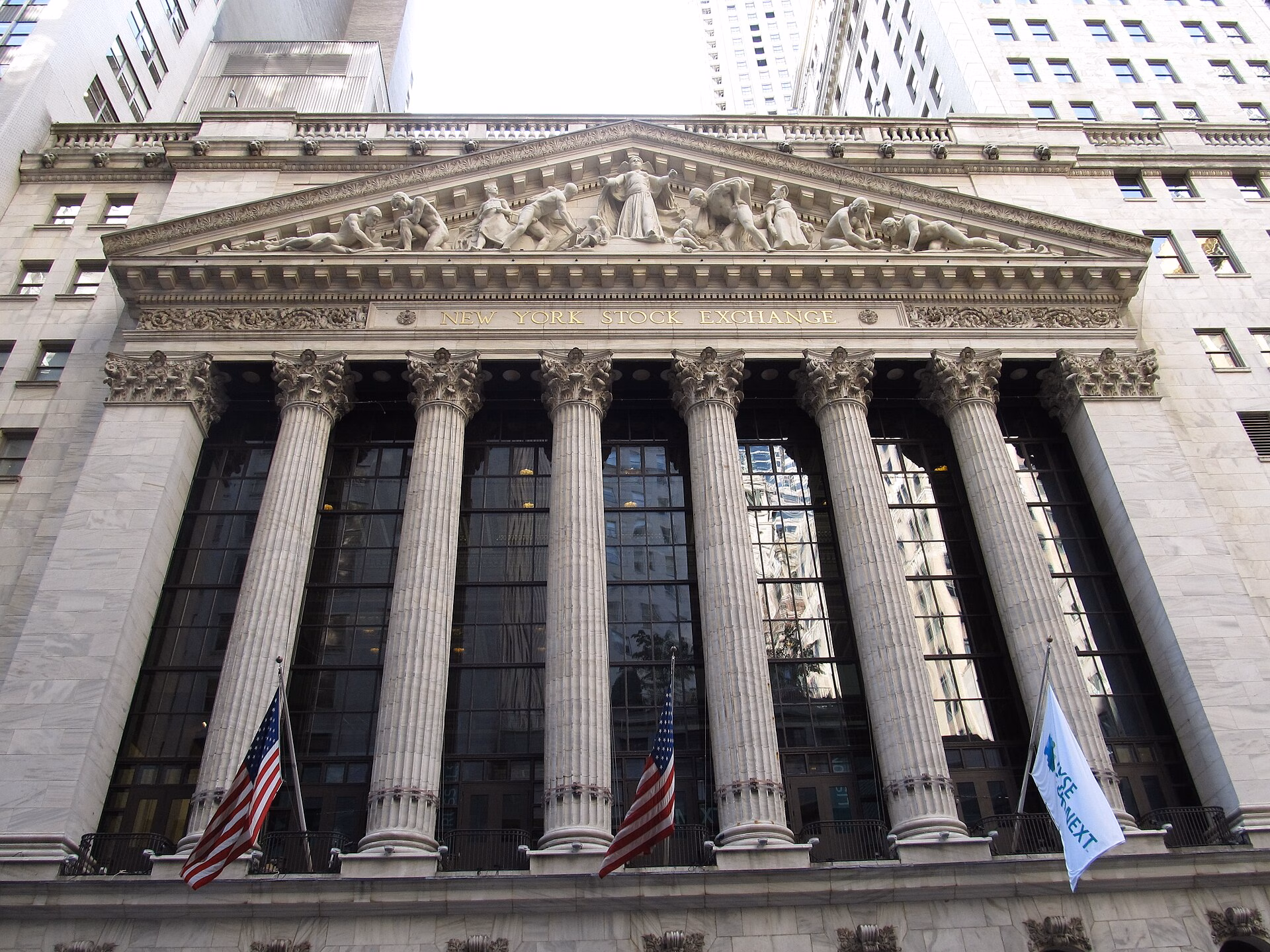 The classical marble facade and colonnade of the New York Stock Exchange at 11 Wall Street in Lower Manhattan, hung with American flags and the NYSE banner