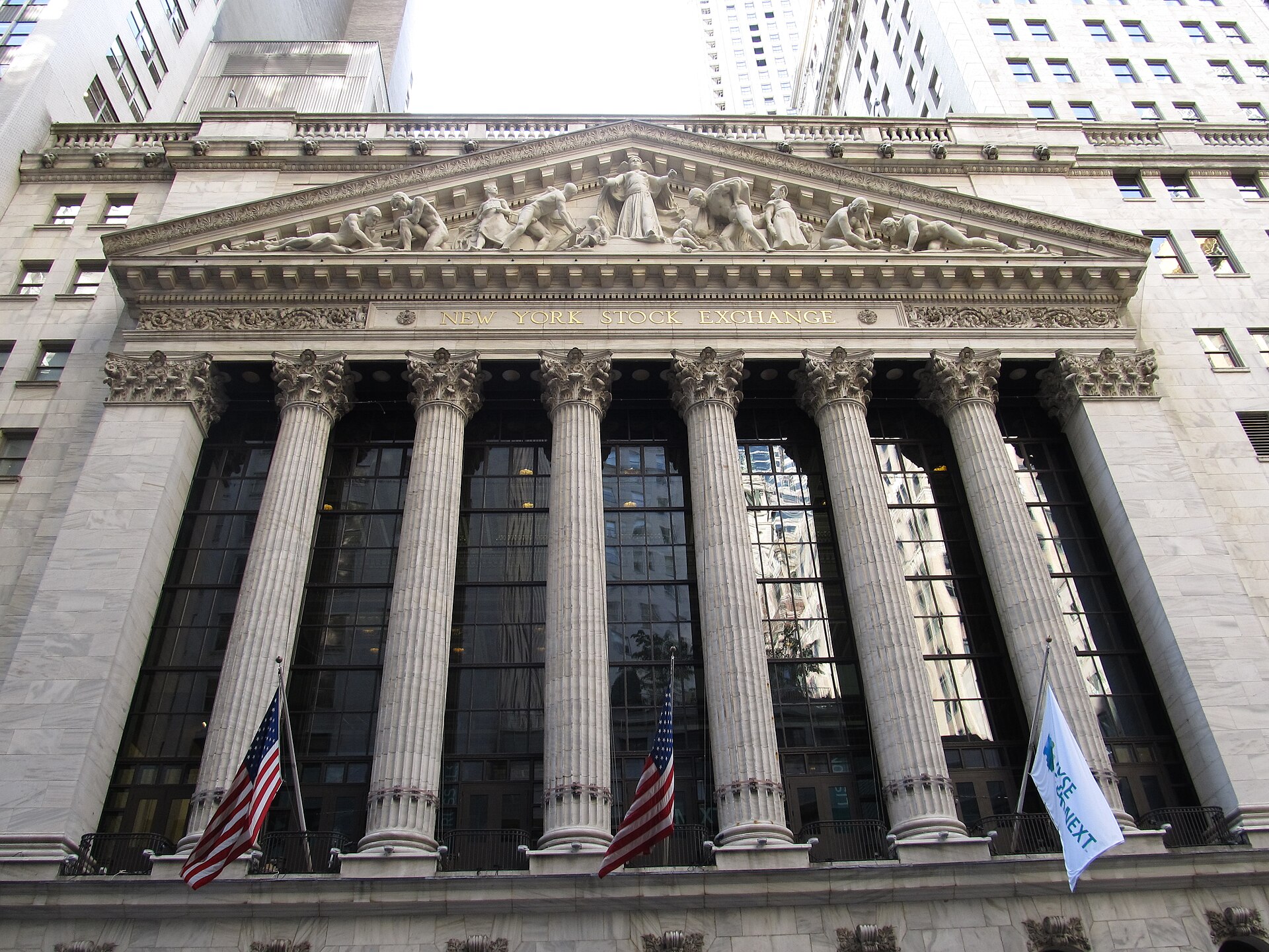 The classical marble facade and colonnade of the New York Stock Exchange at 11 Wall Street in Lower Manhattan, hung with American flags and the NYSE banner