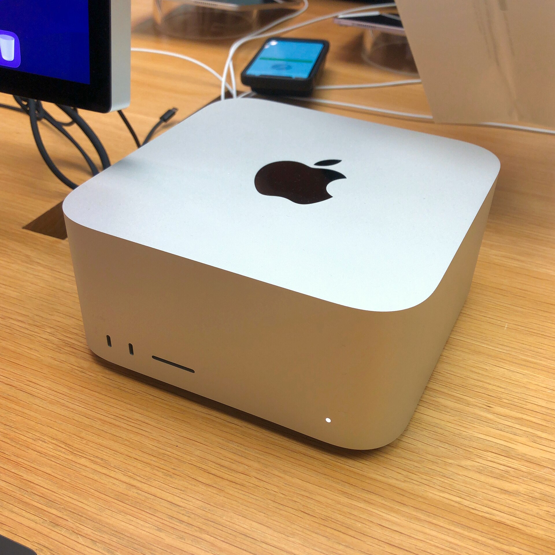 A silver Mac Studio, a small square aluminium desktop computer, photographed on a store display table