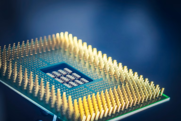 Macro photograph of a computer processor showing its gold contact pins against a dark blue background