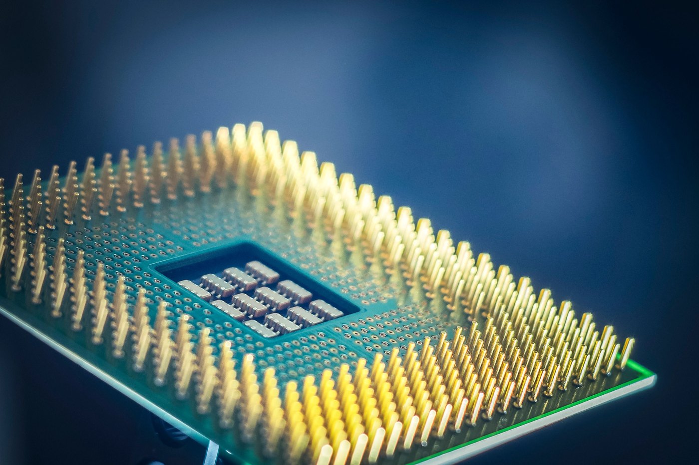 Macro photograph of a computer processor showing its gold contact pins against a dark blue background