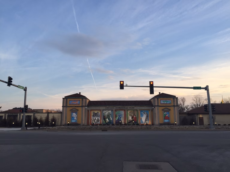 The remodeled north entrance of Brookfield Zoo, photographed at dusk, with colorful animal-mural panels flanking the ticket pavilion and the words 'Chicago Zoological Park' across the facade.