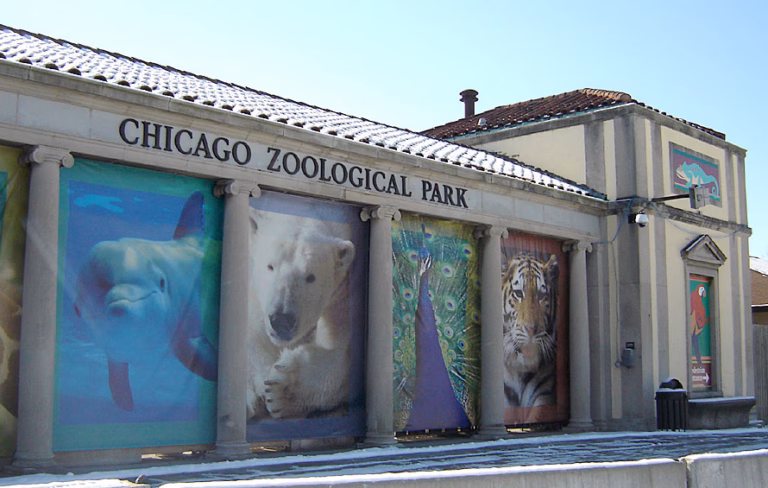The stone entrance gate of Brookfield Zoo Chicago, inscribed Chicago Zoological Park, with large animal banners on the facade
