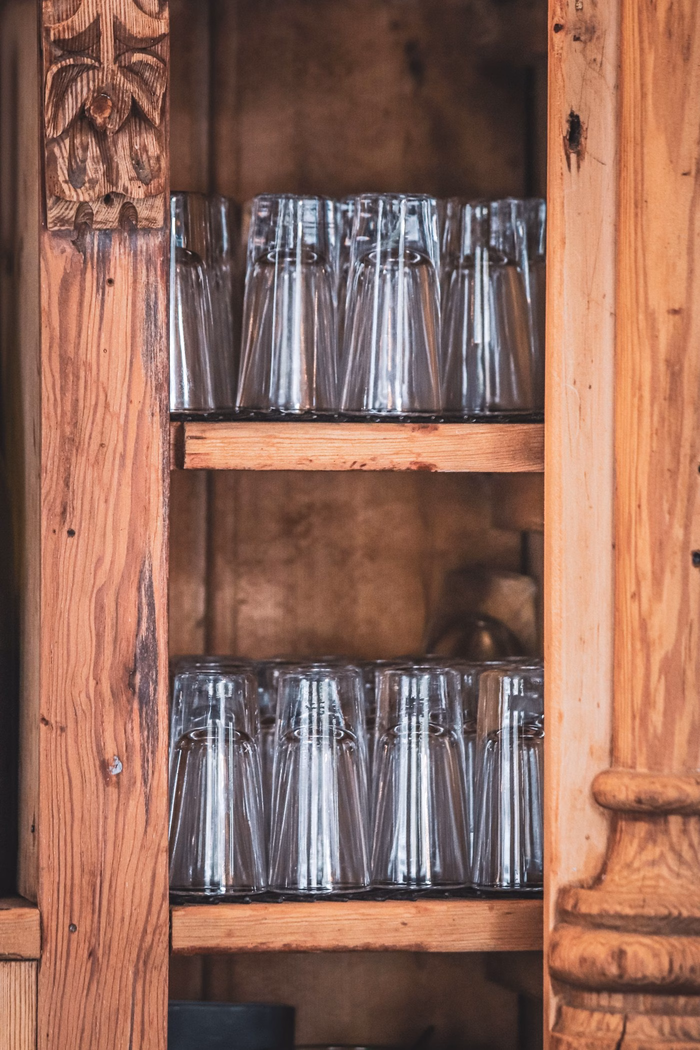 Neatly stacked shot glasses inside a rustic wooden cabinet