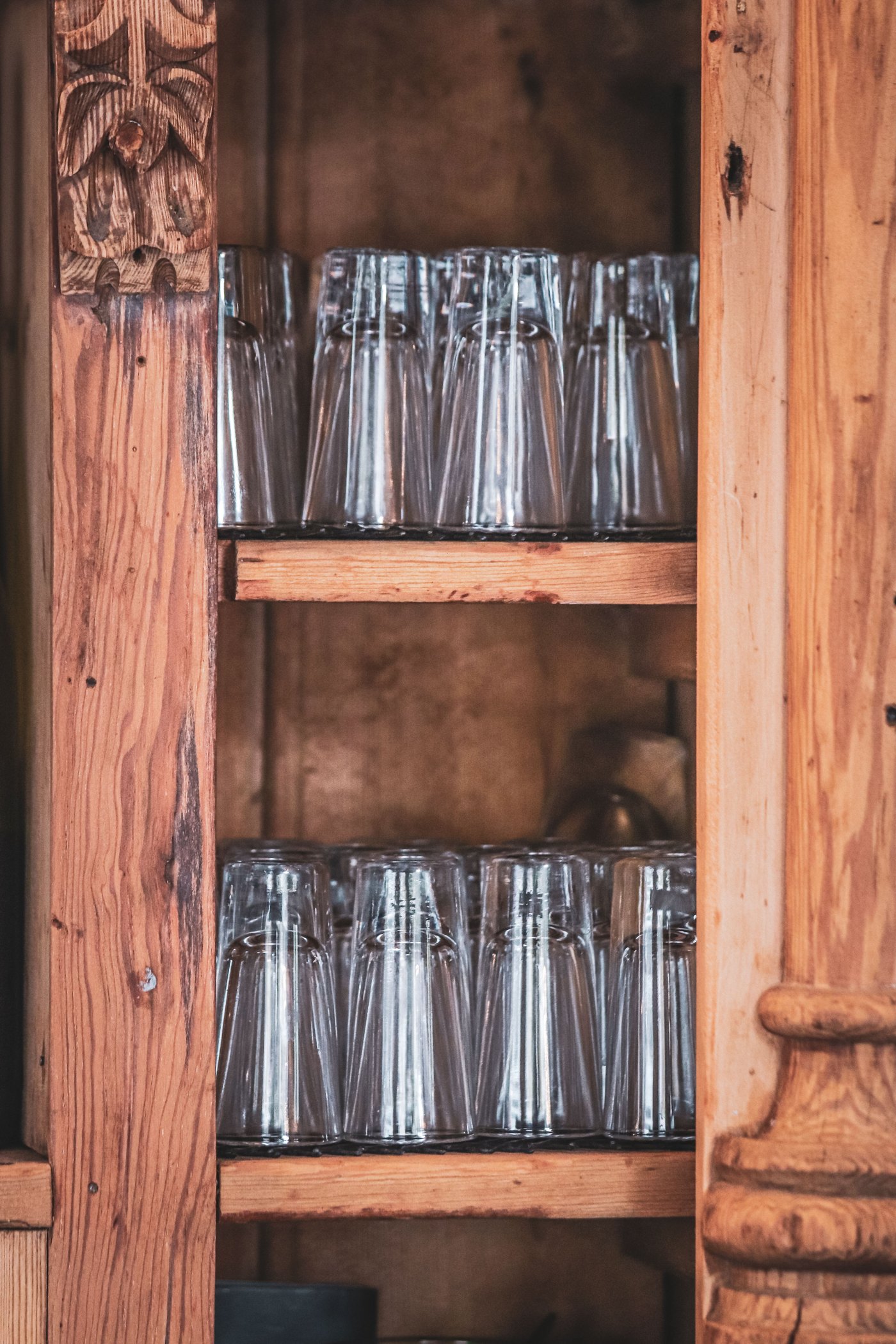 Neatly stacked shot glasses inside a rustic wooden cabinet