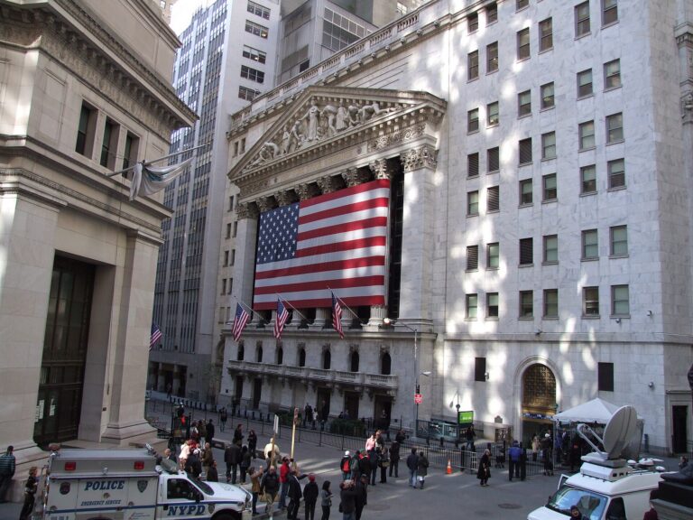 New York Stock Exchange building facade with a large United States flag, viewed from Federal Hall across Broad Street