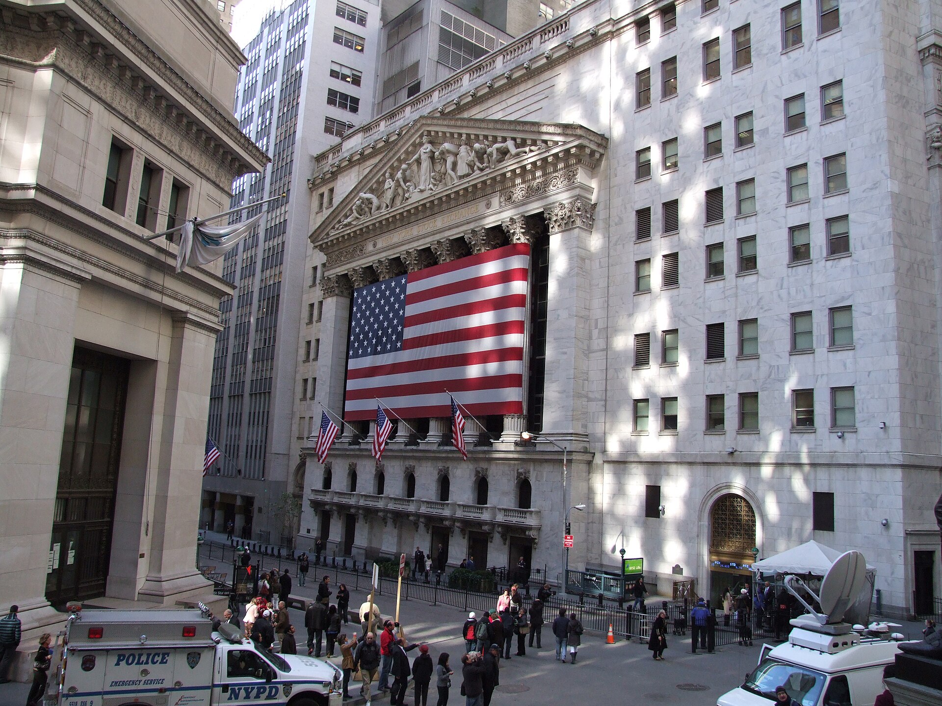 New York Stock Exchange building facade with a large United States flag, viewed from Federal Hall across Broad Street