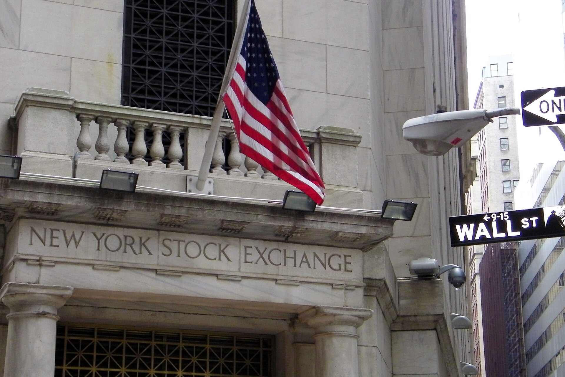 American flag above the New York Stock Exchange entrance beside a Wall Street sign