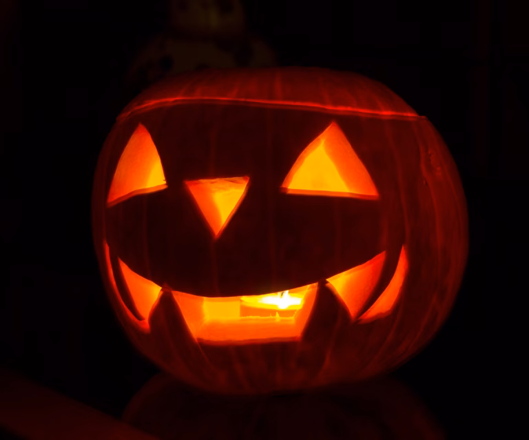 A glowing carved pumpkin (jack-o'-lantern) with a spooky face in the dark.