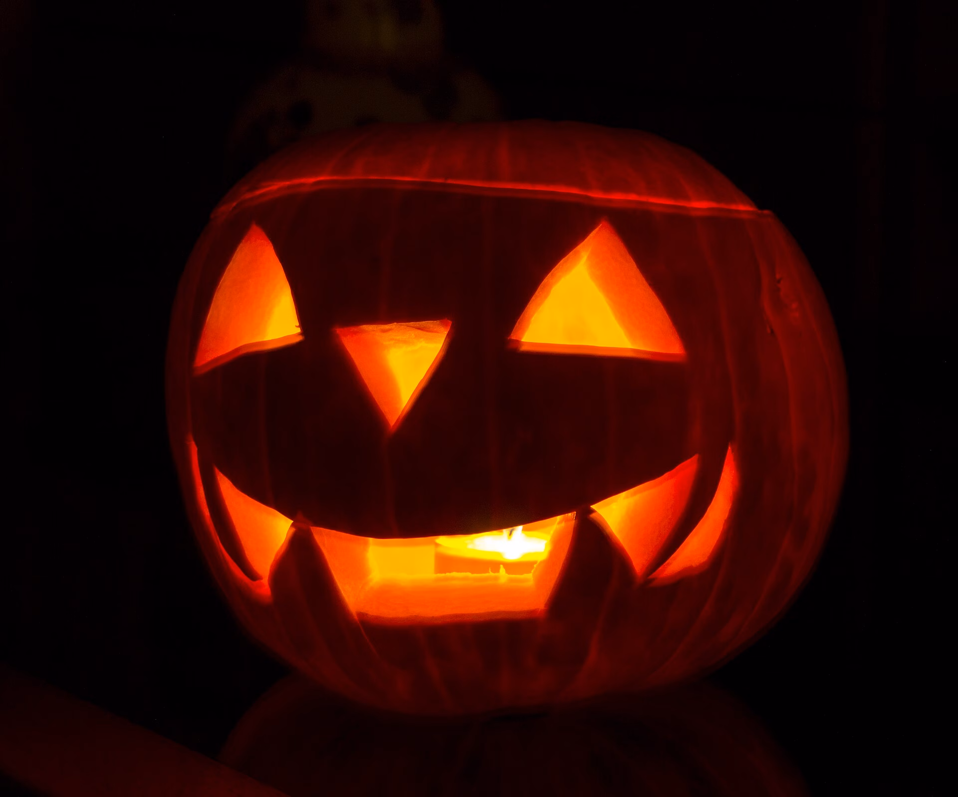 A glowing carved pumpkin (jack-o'-lantern) with a spooky face in the dark.