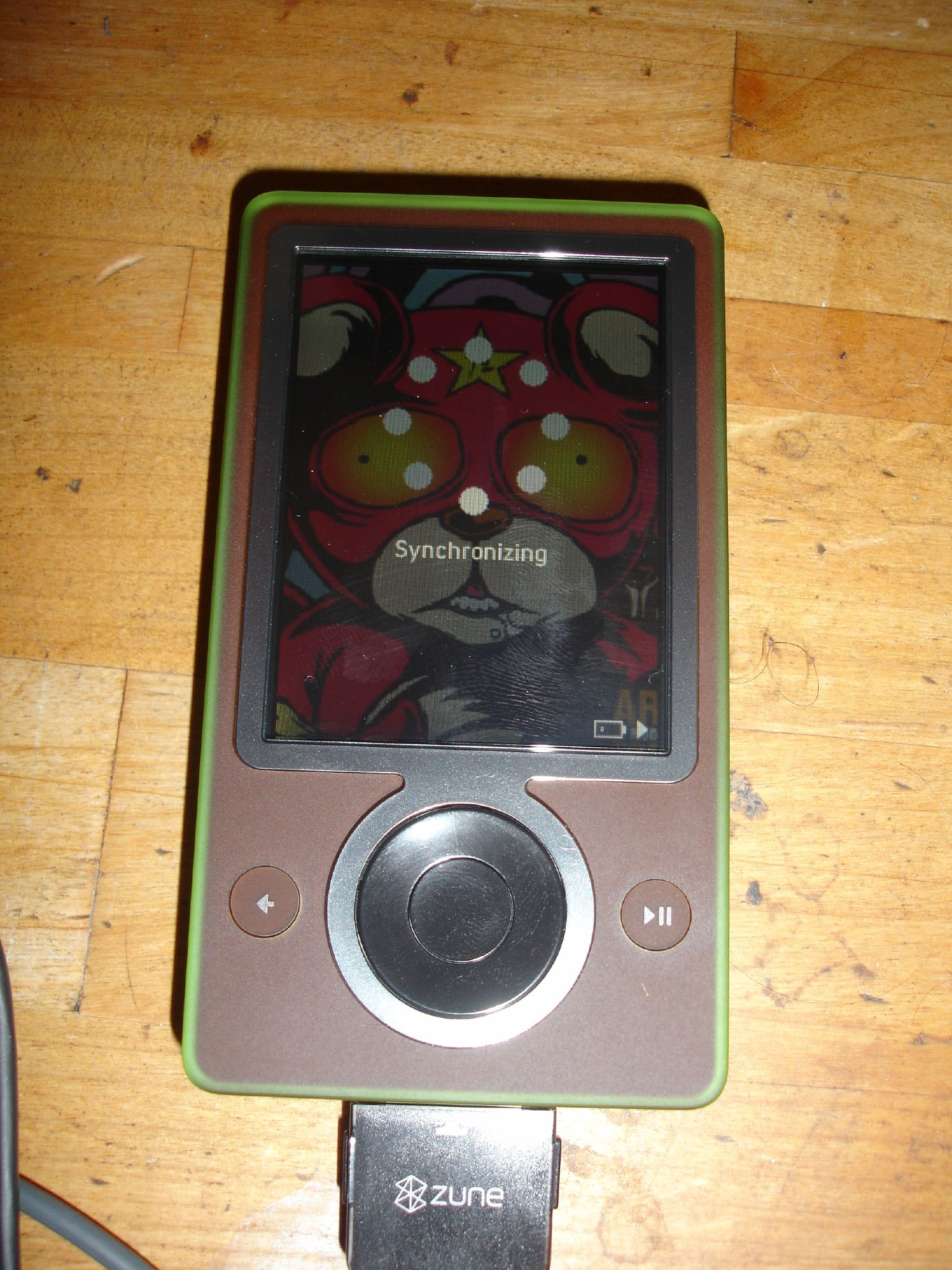 Brown first-generation Microsoft Zune 30 showing a Synchronizing screen and connected to a Microsoft USB sync cable