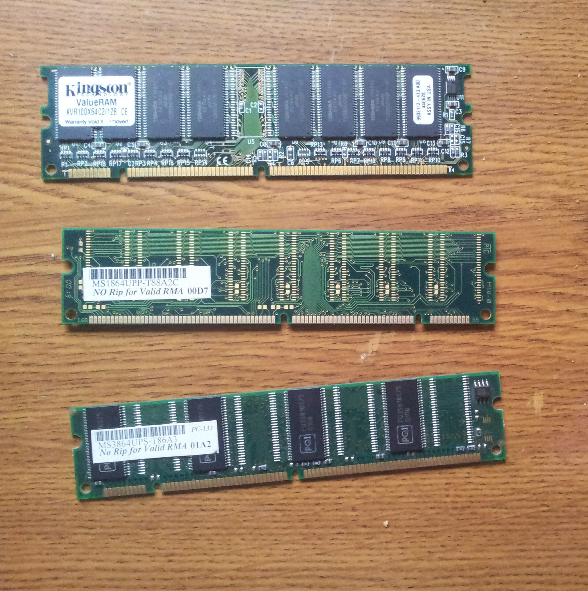 Three green SDRAM memory modules laid out on a wooden surface.